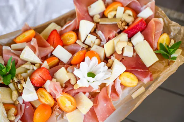 Dilimlenmiş peynirli jamon, parşömen üzerinde meyve ve bal.
