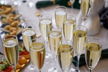 Bir ziyafet salonunda beyaz bir masada şampanya bardakları.