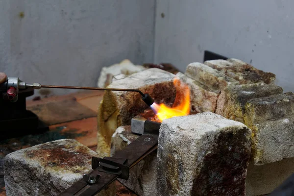A blow torch is used to apply heat to a crucible full of silver to be melted down