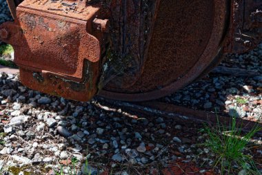 Paslı kahverengi, raylarda paslı bir tekerlek var. Rayların arasında çakıl taşları ve yanında yeşil çimenler var..