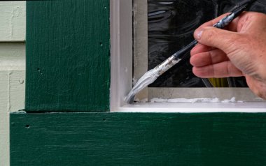 Köşeye yaklaşırken, bir ressam pencere pervazına beyaz bir kat boya sürüyor. Pencereyi korumak için maske bandı kullanıldı.