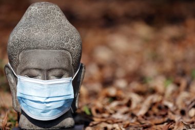 Coronavirus (COVID-19) salgını. Buda heykeli beyaz tıbbi yüz maskesi. 