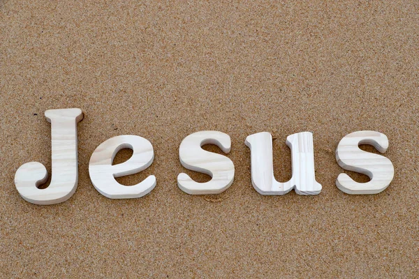 在沙滩沙地的背景上形成耶稣这个字的木制字母 基督教符号 — 图库照片