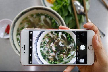 Bir kase Vietnam erişte çorbası, Pho olarak bilinir. Kadın akıllı telefonuyla yemeğinin fotoğrafını çekiyor. Ho Chi Minh Şehri. Vietnam.