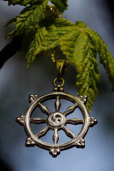 Buddhism Dharma wheel pendant necklace on a young green leaf.  Religious symbol.