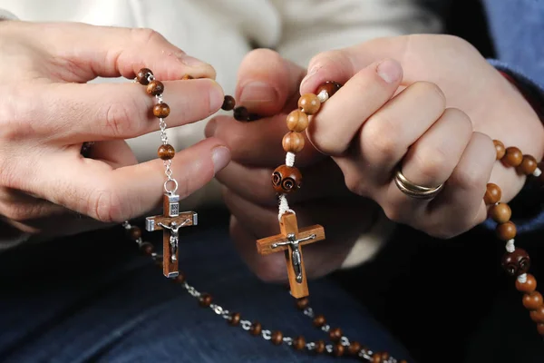 Catholic man and woman praying together at home. Close up on hands with prayer beads.   France.