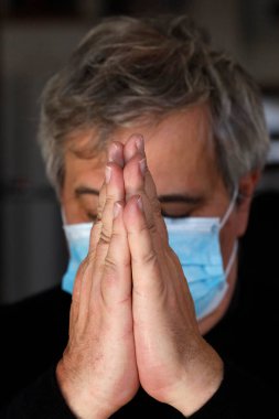 Coronavirüs salgını (COVID-19). Koruyucu maske takan adam dua ediyor.  