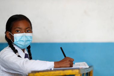 Ortaokul. Sınıfta cerrahi maske takan bir kız. Nepal. 