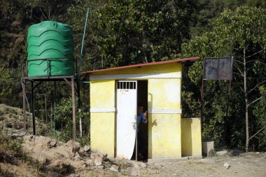 Okul bahçesindeki temel tuvalet bloğu. Tuvaleti kullanan çocuk. Nepal. 