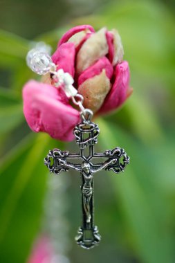 Pembe bir rhododendron çiçeğinin üzerinde İsa 'nın olduğu Katolik tespihi. Ekoloji ve dini kavram.