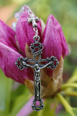 Pembe bir rhododendron çiçeğinin üzerinde İsa 'nın olduğu Katolik tespihi. Ekoloji ve dini kavram.