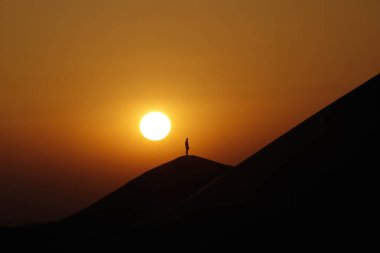 Kum tepeciğindeki siluet. Çölde günbatımı meditasyonu. Din, inanç, dua ve maneviyat kavramı.