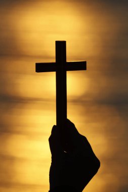 Hristiyan bir kadın günbatımında bir haç tutuyor. Ellerinizi kapatın. Din, inanç, dua ve maneviyat kavramı.