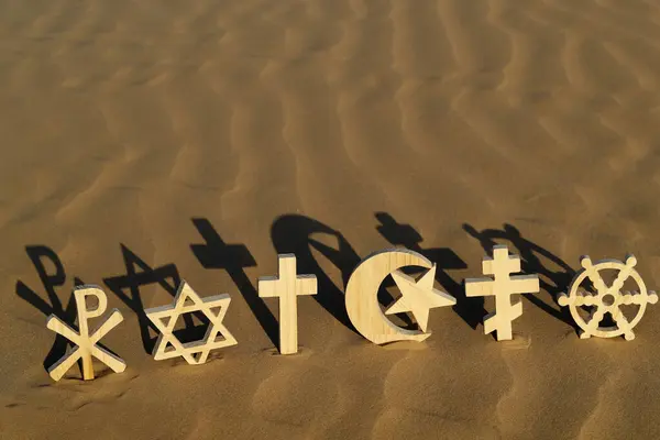 stock image Religious symbols on sand at sunset :  Catholic, Islam, Judaism, Orthodoxy, Protestant, Buddhism and Hinduism. Interreligious, interfaith and spirituality concept.