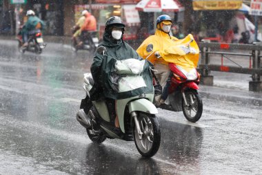 Vietnamlılar kask takıyor ve yağmurluklarla motosiklete biniyor sağanak yağmurda, sokaklarda su var. Saigon 'da yağmur mevsimi, Ho Chi Minh şehri. Vietnam. 