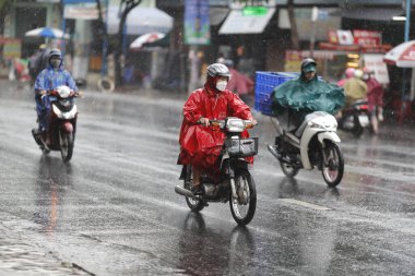 Vietnamlılar kask takıyor ve yağmurluklarla motosiklete biniyor sağanak yağmurda, sokaklarda su var. Saigon 'da yağmur mevsimi, Ho Chi Minh şehri. Vietnam. 