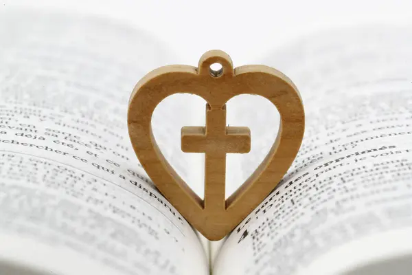 Open bible with wooden heart with christian cross. Love and religion concept.