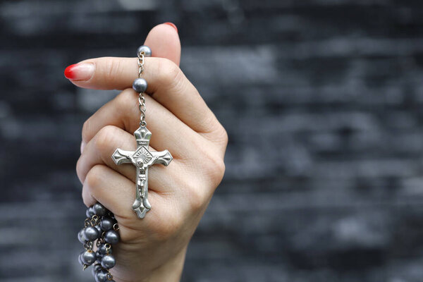 Woman praying with a silver crucifix and a rosary with beads.  Concept for religion, faith and prayer,