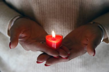 Katolik kilisesinde kalp şeklinde yanan kırmızı bir mum tutan bir kadın eli. İnanç ve spritüellik kavramı. Fransa.