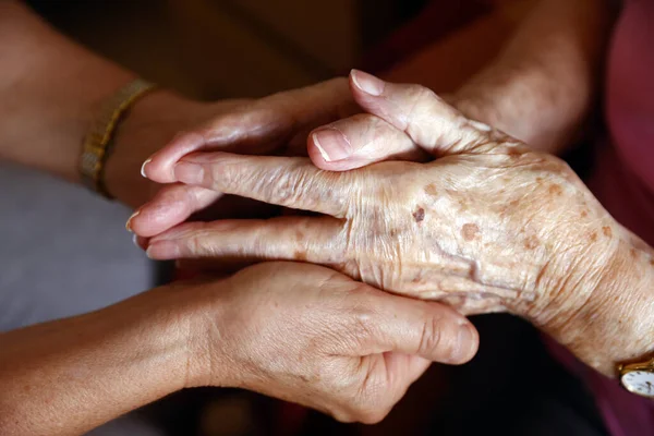 Retirment home.  Close up of care assistants hand reassuring senior woman.