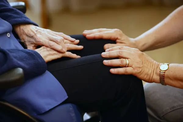 Retirment home.  Close up of care assistants hand reassuring senior woman.