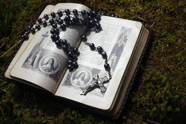 Old Bible and  catholic rosary beads on wood. 