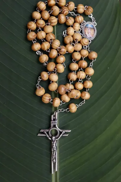 Rosary or prayer beads on a green leaf. Jesus on the cross. Crucifix.