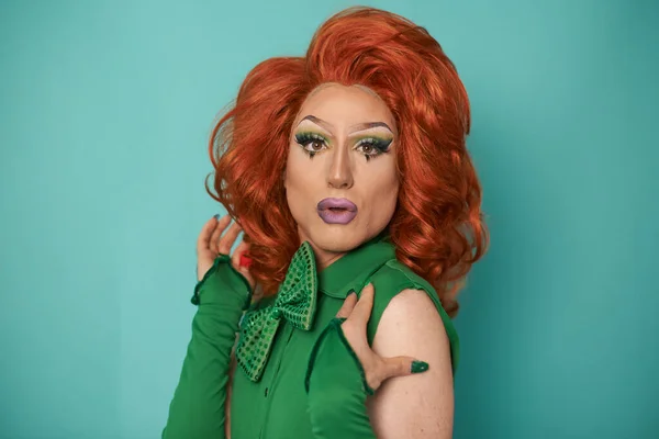Side view of transgender male model in stylish feminine bodysuit with LGBT rainbow flag looking at camera while standing in studio against blue background