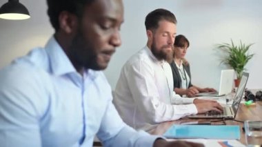 Gerçek zamanlı olarak sakallı bir adamın ofiste kadınlarla netbook üzerinde çalışırken iş projesini siyahi bir iş arkadaşına açıklaması.