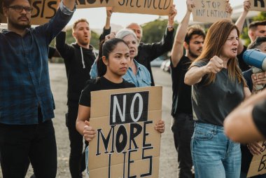 Bir grup çok ırklı protestocu, günlük giysiler ve karton pankartlarla sokakta dikilip isyan sırasında hoparlörlere bağırıyorlar.