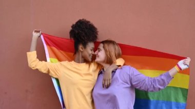 Lezbiyen çiftin, rüzgarlı bir günde burunlarını sarıp, LGBT bayrağına sarılıp nazikçe öpüştüğü ve siyahi bir kadının kız arkadaşının saçlarına dokunduğu gerçek bir zaman.