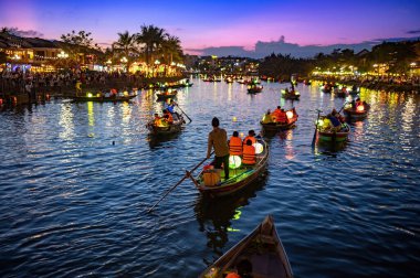 Akşamları tropikal kırsal kesimde karnaval ışığı altında sakin nehirde güneşli gökyüzüne karşı savaşan, tanınmayan grup insanlarının arka planı.