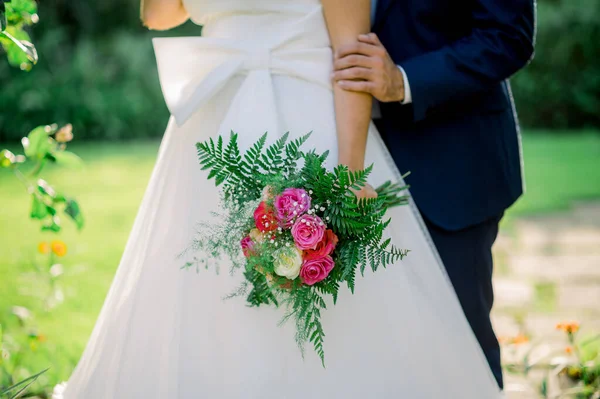 Жених Черном Костюме Обнимает Элегантную Невесту Белом Платье Букетом Розовых — стоковое фото