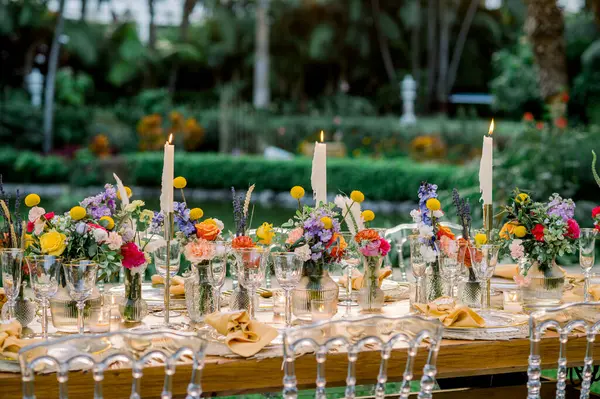 Yanan mumlar ve canlı çiçeklerle dolu ahşap masa. Eko otelinin tropikal bahçesinde düğün için hazırlanıyor.