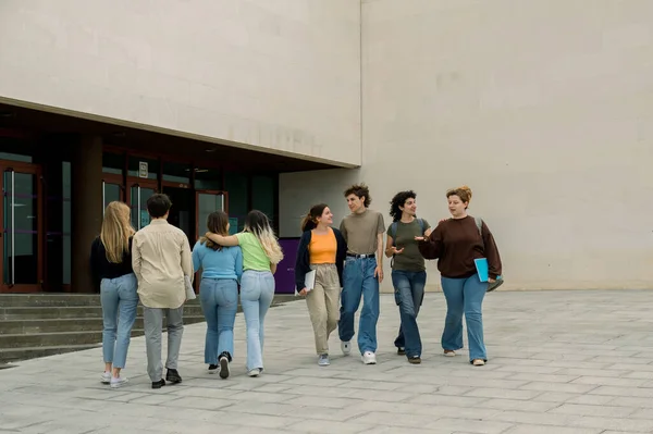 カジュアルな服装をしたフレンドリーな若い多人種の学生は 大学の建物の中を歩いている間に笑顔で話し 一緒に自由な時間を過ごす — ストック写真