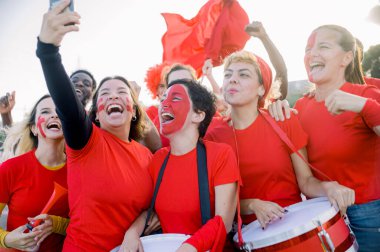 Sırt çantalı, neşeli, genç bir grup. Sırt çantalı, gülümseyen ve birlikte eğlenirken akıllı telefondan selfie çeken.