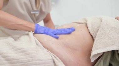 Vücut düzeltme işleminden önce güzellik kliniğindeki müşterinin şişko karnına masaj yapan yüzü olmayan bir uzman.
