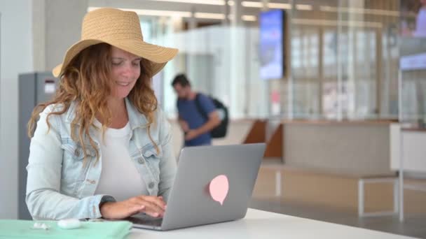 穿着休闲装的年轻女子 拿着笔记本电脑坐在机场的一张桌子旁 正在做一个项目 — 图库视频影像