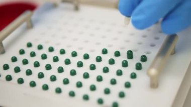 Yüksek açılı el kamerası görüntülerinde mavi eldivenli isimsiz bilim adamı laboratuvarda kişiselleştirilmiş haplar yaparken beyaz ve yeşil kapsülleri dolduruyor.