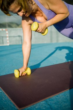 Spor giyim bölümünde spor salonunda spor yaparken yüksek açılı kadın sporcu spor yaparken dambıllarla egzersiz yapıyor.