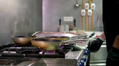 Gerçek zamanlı olarak, lateks eldivenli isimsiz erkek aşçı kızartma tavalarında yemek pişirirken profesyonel restoranda müşteriler için lezzetli yemekler hazırlıyor.