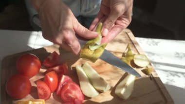 Yüksek açılı el kamerasıyla çekilmiş, isimsiz bir kadın armudu tahta kesme tahtasıyla soyarken mutfakta sağlıklı atıştırmalıklar hazırlıyor.