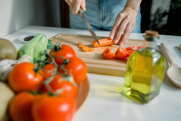 Evde yemek pişirirken domatesli ve otlu sağlıklı salata hazırlarken mutfakta havuç doğrayan isimsiz bir ev hanımı.