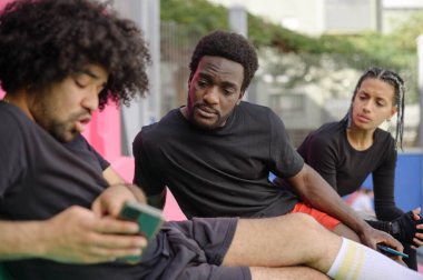 Spor giyim sektöründe Afro-Amerikalı erkek ve bayan sporcular cep telefonlarını paylaşıyor ve sosyal medyayı tarıyor.