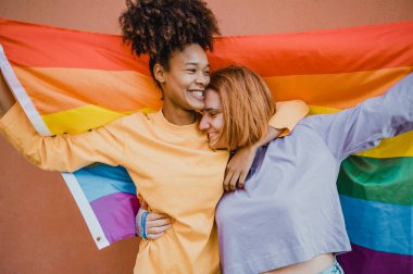 Sokakta bej arka planda LGBT bayrağı taşıyan pozitif, çok ırklı lezbiyen çift