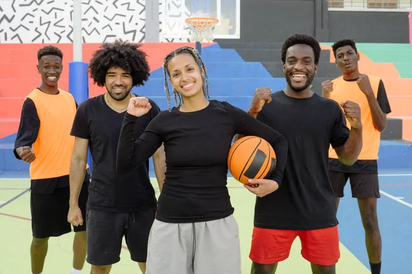 Afro-Amerikalı kadın ve erkek basketbolcular yumruklarını sıkmış ve şehirde spor sahasında zaferi kutluyorlar.