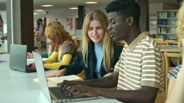 Sınav hazırlıkları sırasında bilgisayarda yazı yazarken kız arkadaşıyla gülümseyen ve konuşan gündelik giyinmiş Afro-Amerikalı genç bir öğrenci.