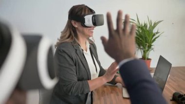 Sanal gerçeklik bardaklarını kullanan neşeli çeşitli ofis çalışanları ve ofiste online toplantı yaparken el sallıyorlar.