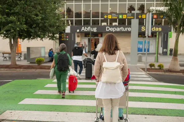 Sırt çantalı, sırt çantalı, yaya geçidinde yürüyen ve havalimanı kalkış bekleme odasına yaklaşan anonim uçak yolcularının arka görüntüsü