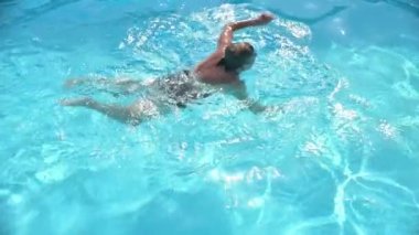 Yaz günü dinlenme yerindeki temiz su havuzunda yüzen mayolu olgun bir kadının yavaş hareketi.